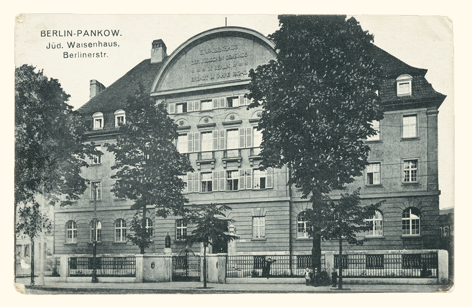 2008_311_53001 1 - Waisenhaus Pankow Historisches Gebäude des jüdischen Waisenhauses in Berlin-Pankow, umgeben von Bäumen und einem Zaun.