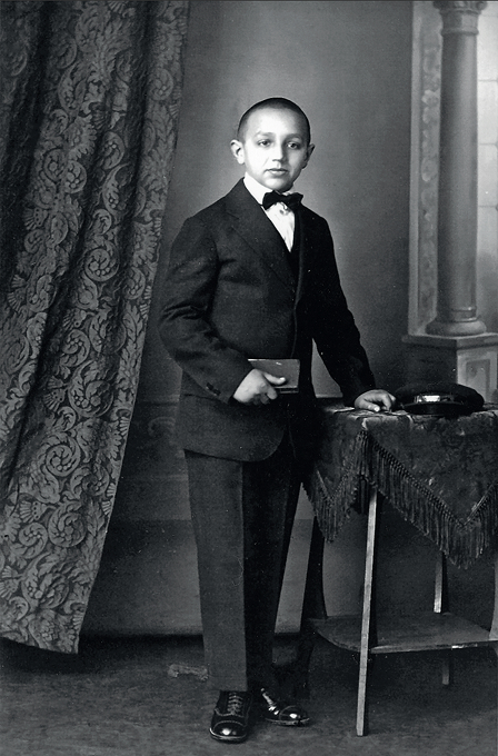 Alex Deutsch - Waisenhaus Pankow Ein junger Junge in einem Anzug mit Fliege steht neben einem Tisch, auf dem ein Hut und eine kleine Kiste liegen.