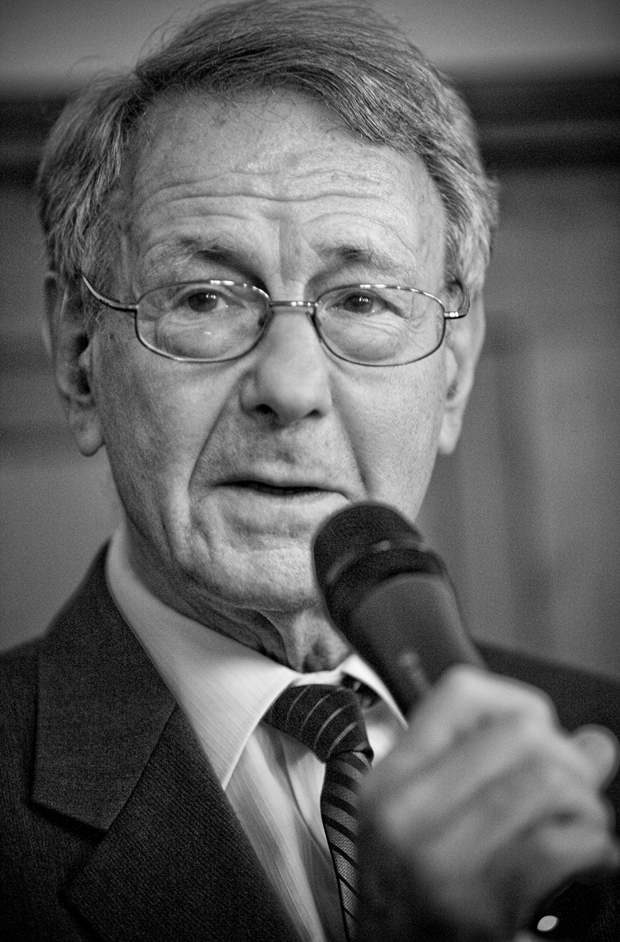 Leslie Baruch Brent - Waisenhaus Pankow Älterer Mann mit Brille spricht in ein Mikrofon, trägt einen Anzug und hat graue Haare.