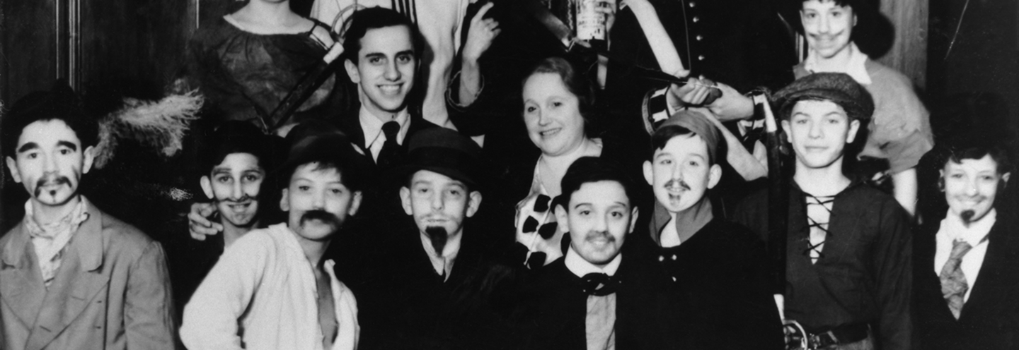 Gruppenszene mit Männern und Frauen in historischen Kostümen, lächelnd, vor einem Hintergrund aus der Vergangenheit.