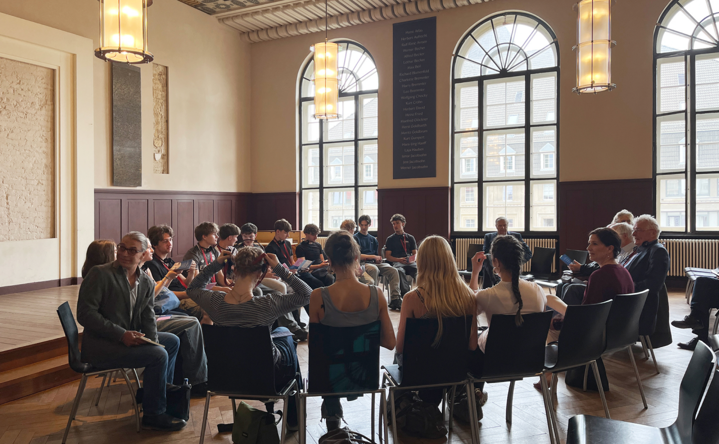 Gruppendiskussion in einem hellen Betsaal mit großen Fenstern und Stuhlkreis. - Waisenhaus Pankow Gruppendiskussion in einem hellen Betsaal mit großen Fenstern und Stuhlkreis.